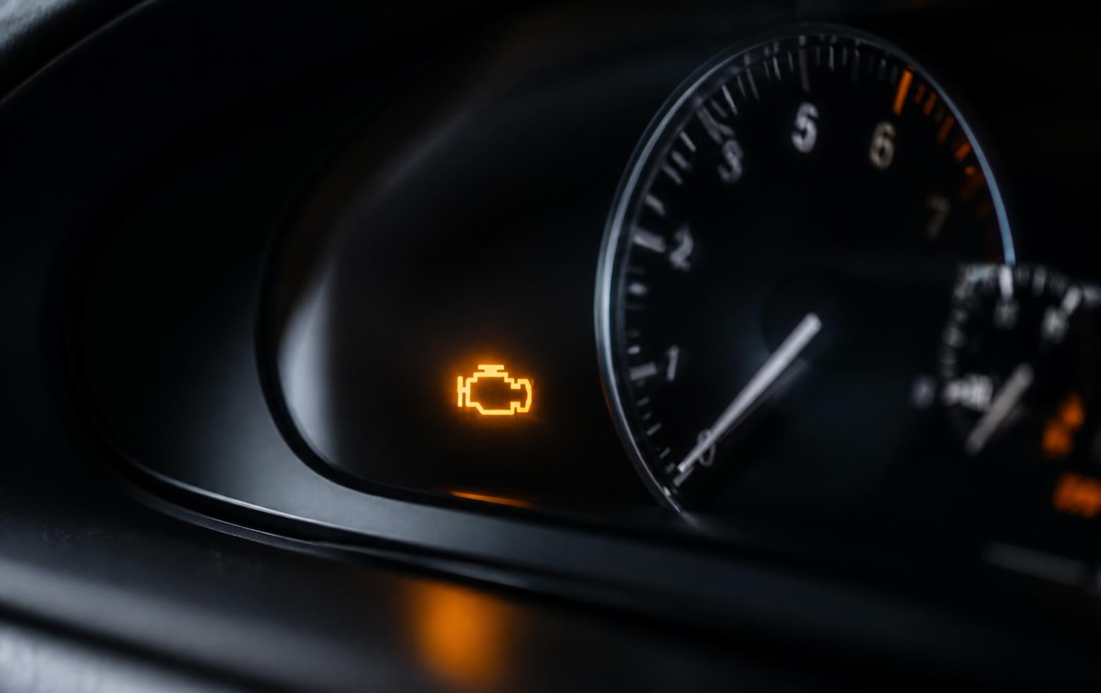 Illuminated check engine warning light on a dark car instrument cluster